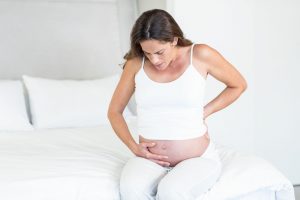 45529085 - unhappy pregnant woman suffering from back pain sitting on bed